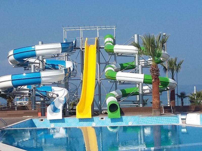 Scivoli d'acqua blu, gialli e verdi vicino a una piscina con palme e cielo sereno.