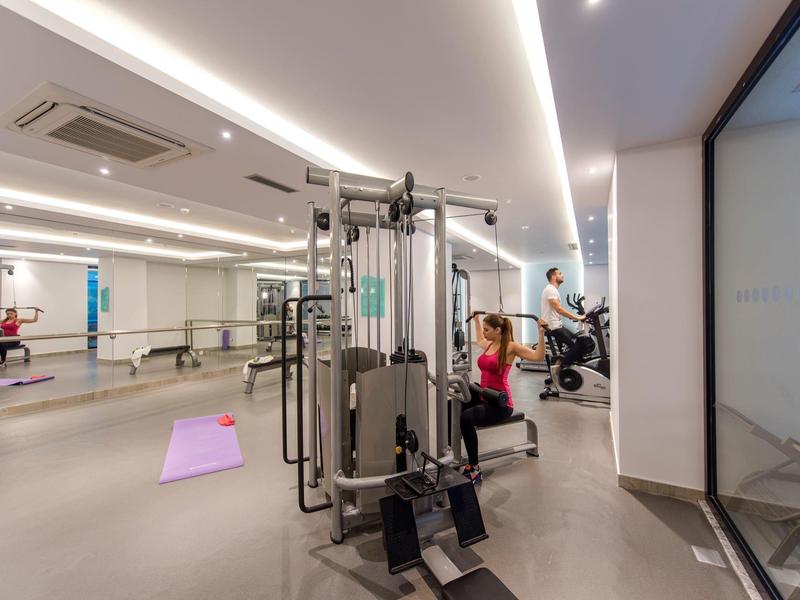 Palestra moderna in hotel con attrezzi, tappetino rosa e ampie finestre.