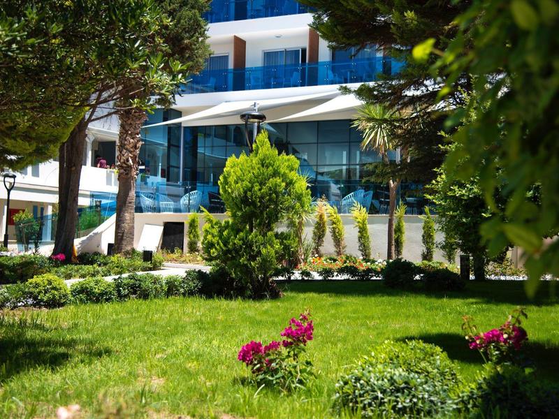 Giardino verde con fiori e alberi davanti a un hotel moderno con balconi