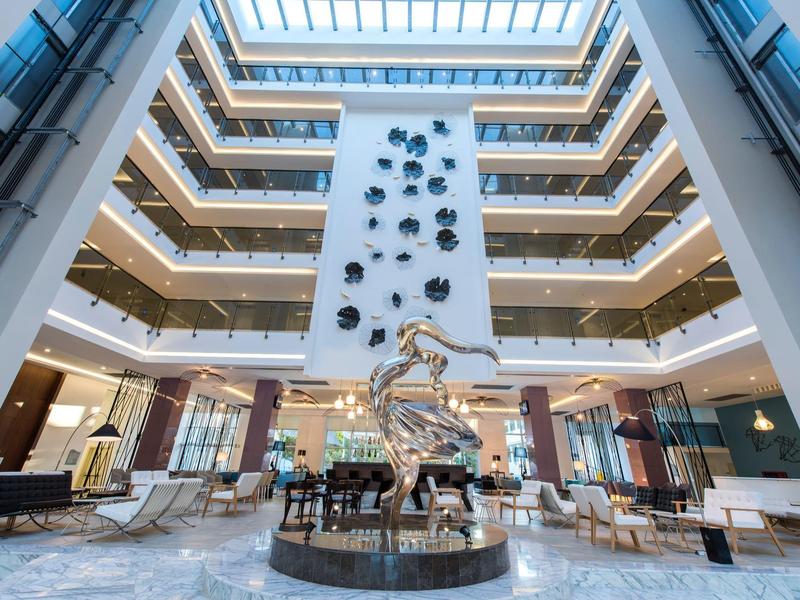 Atrio moderno dell'hotel con una scultura centrale d'argento e più piani visibili con balconi.