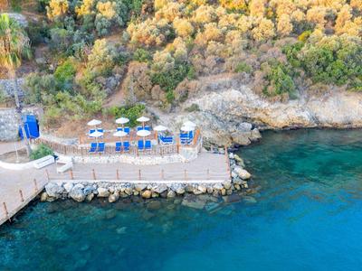 Malý mol s deštníky a židlemi u průzračného moře vedle skalnatého pobřeží a lesa