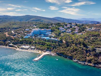 Letecký pohled na přímořský hotel s molem, obklopený zalesněnými kopci.