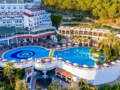 Hotel s dvěma velkými venkovními bazény, obklopený lehátky a zelenou krajinou.