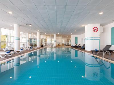 Vnitřní bazén s modrými dlaždicemi, lehátky a velkými okny pro přirozené světlo