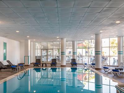 Vnitřní hotelový bazén s lehátky a velkými okny.