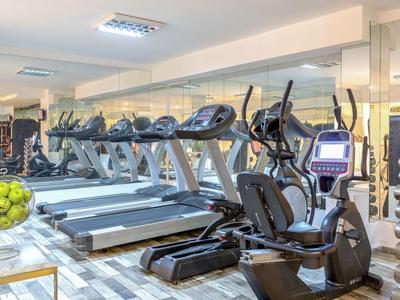 Siłownia z bieżniami, rowerami eliptycznymi i ciężarami w jasnym pomieszczeniu.