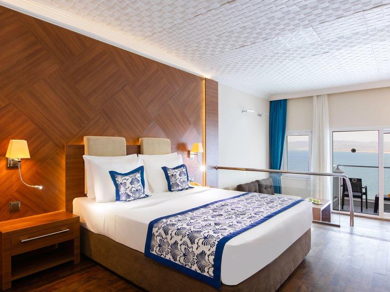 Moderní hotelový pokoj s velkou postelí, dřevěnou akcentní stěnou a výhledem na terasu.