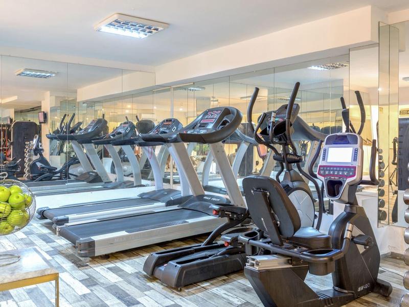 Moderní posilovna s běžeckými pásy, eliptickými trenažéry a výhledem na tenisové kurty.