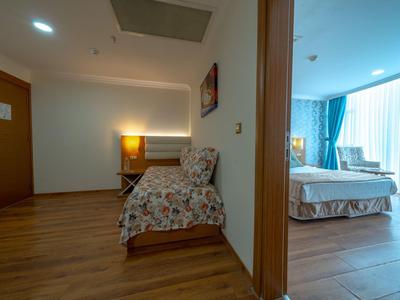 Hotel room with wooden floor, patterned chair, and bed near large window with blue curtains.