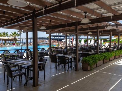 Shaded poolside dining area with tables, chairs, and ocean view.