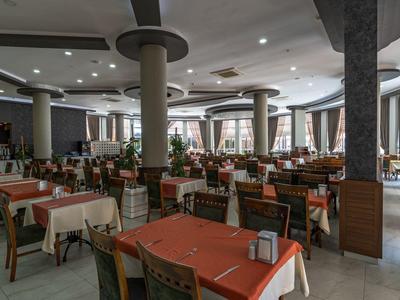 Spacious hotel dining room with numerous tables covered in red and white tablecloths and green chairs.