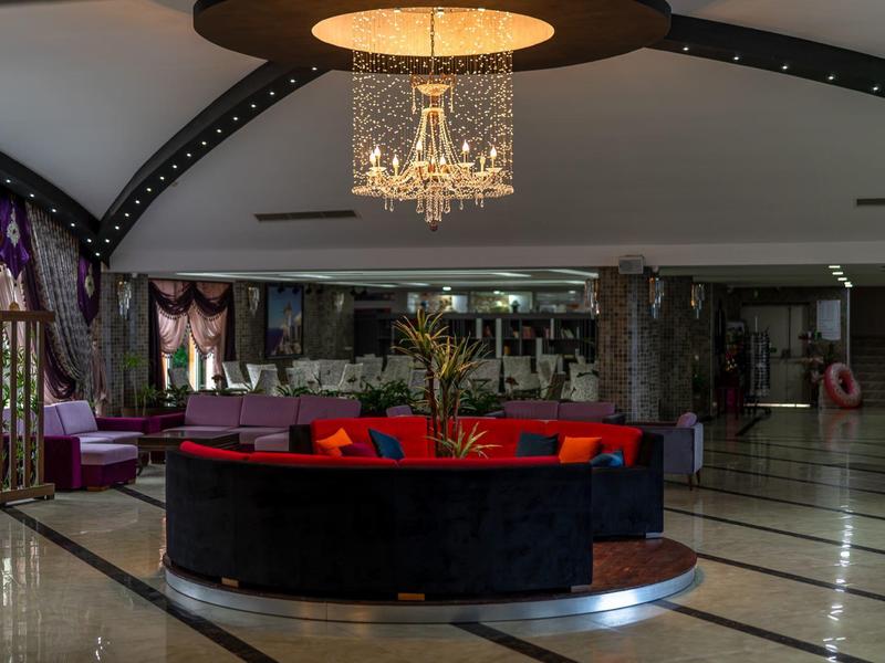 Luxurious hotel lobby with chandelier, circular sofa, and polished marble floor under curved ceiling beams.