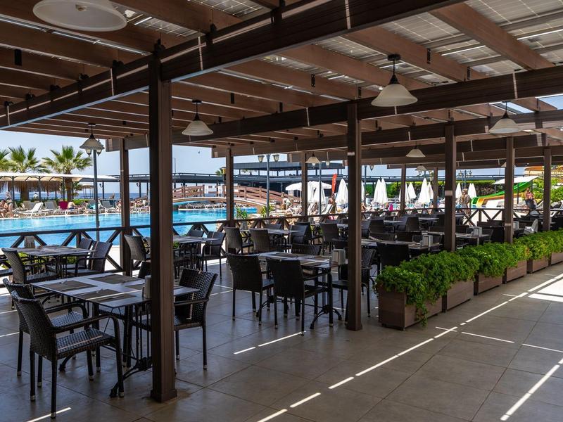 Shaded poolside dining area with tables, chairs, and ocean view.