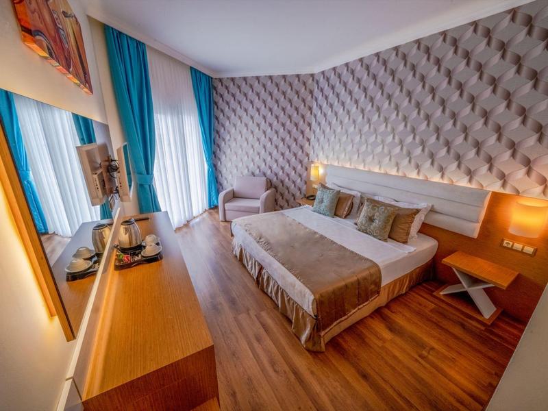 Cozy hotel room with a double bed, patterned wallpaper, blue curtains, and wooden furniture.