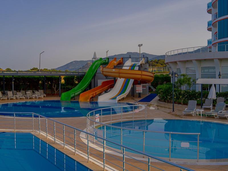 Outdoor pool with colorful water slides and lounge chairs at a hotel under a clear sky.