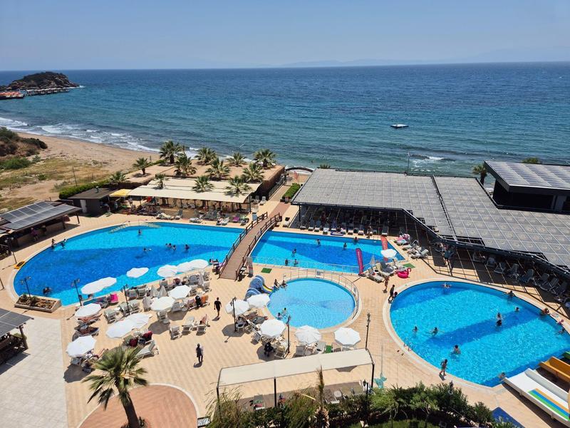 Oceanfront hotel pool area with multiple pools, sunbeds, umbrellas, and palm trees under clear skies.