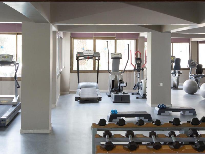 Salle de sport lumineuse avec tapis de course, vélos d'appartement, haltères et ballons de gym.