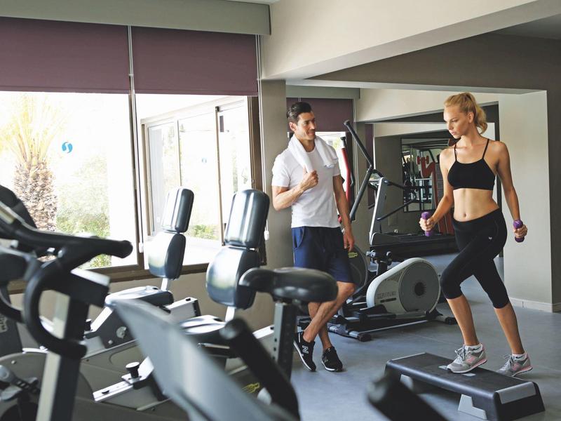 Deux personnes s'entraînent dans une salle de sport moderne avec divers équipements.