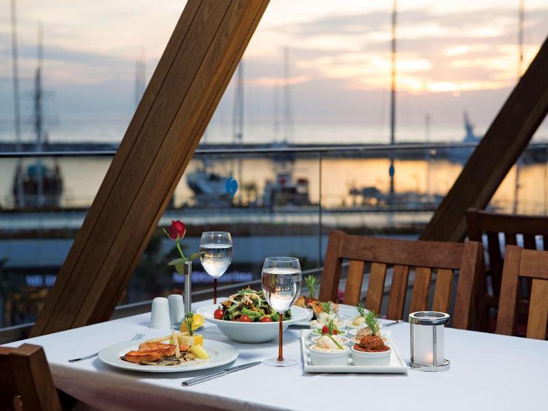 Une table dressée sur une terrasse avec vue sur un port au coucher du soleil
