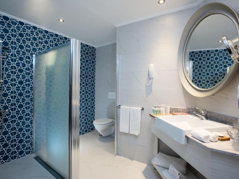 Salle de bain d'hôtel moderne avec lavabo blanc, miroir rond et accents bleus.