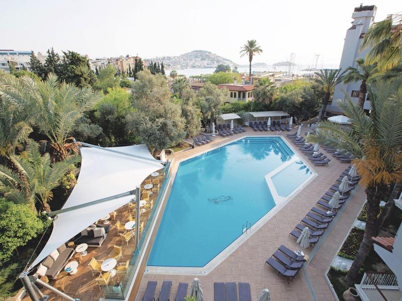 Vue sur une grande piscine propre avec des chaises longues et des palmiers dans un complexe hôtelier.