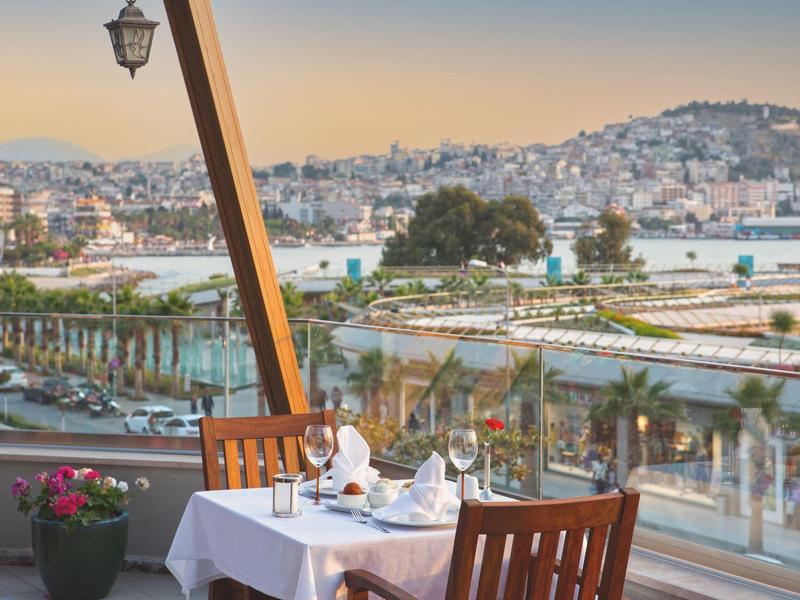 Restaurant avec table dressée sur terrasse avec vue sur la ville et les collines au coucher du soleil.