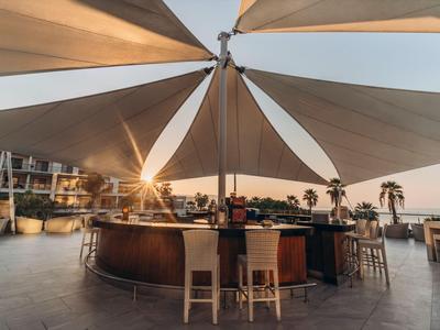 Outdoor-Bar mit großem weißem Sonnensegel und Sonnenuntergang am Hotelpool.