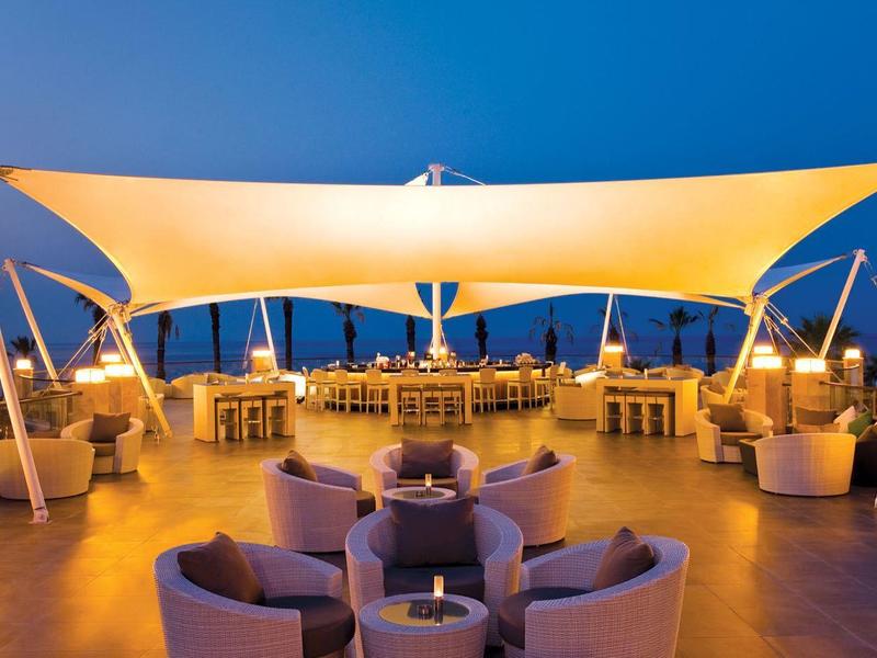 Moderne Dachterrasse bei Abenddämmerung mit orange beleuchtetem Sonnensegel und runden Sitzgruppen.