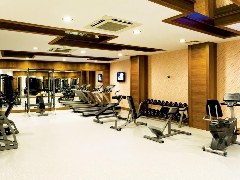 Moderne Fitnessstudio mit Hanteln, Laufbändern und Fahrradergometern, helle Wände und Deckenbeleuchtung.