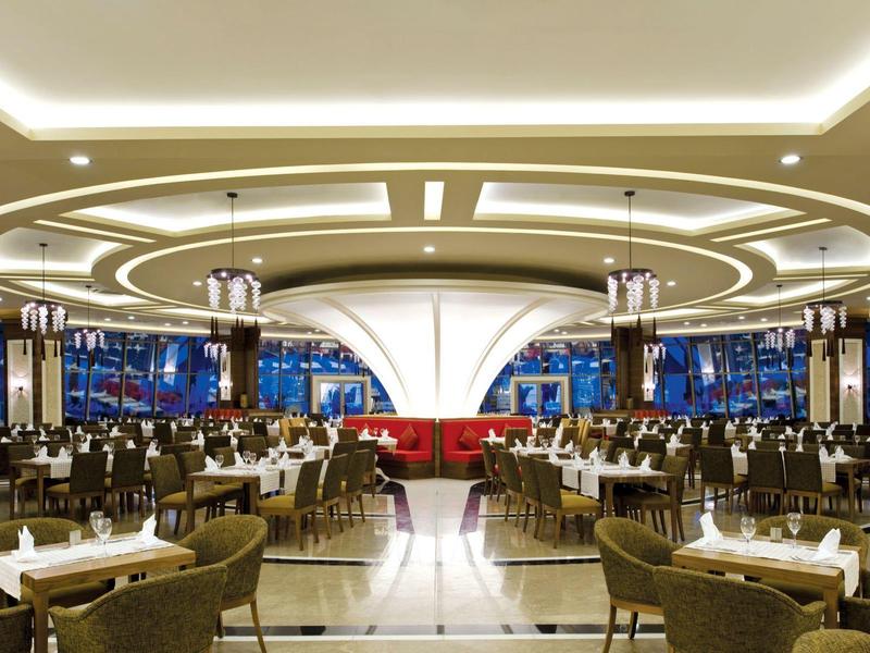 Großer runder Speisesaal mit modernen Kronleuchtern, weißen Tischen und roten Sitzbänken.