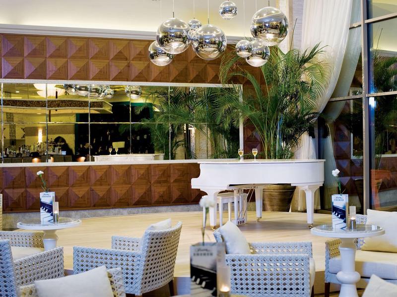 Moderner, eleganter Innenraum mit weißem Flügel, weichen Sesseln und glänzenden Kugelleuchten.