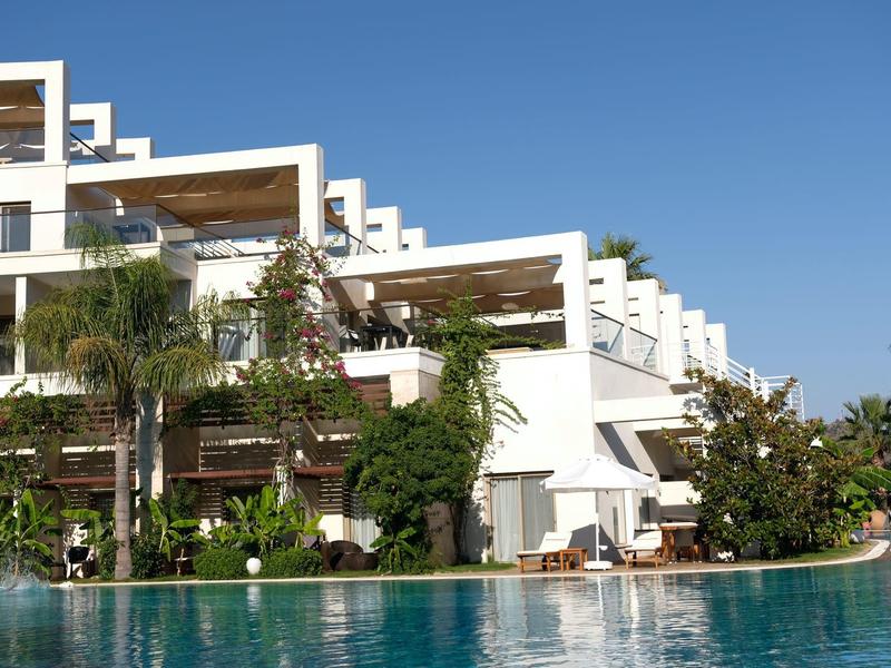 Modernes, weißes Hotel mit terrassenförmigen Balkonen und großem Pool bei klarem Himmel.