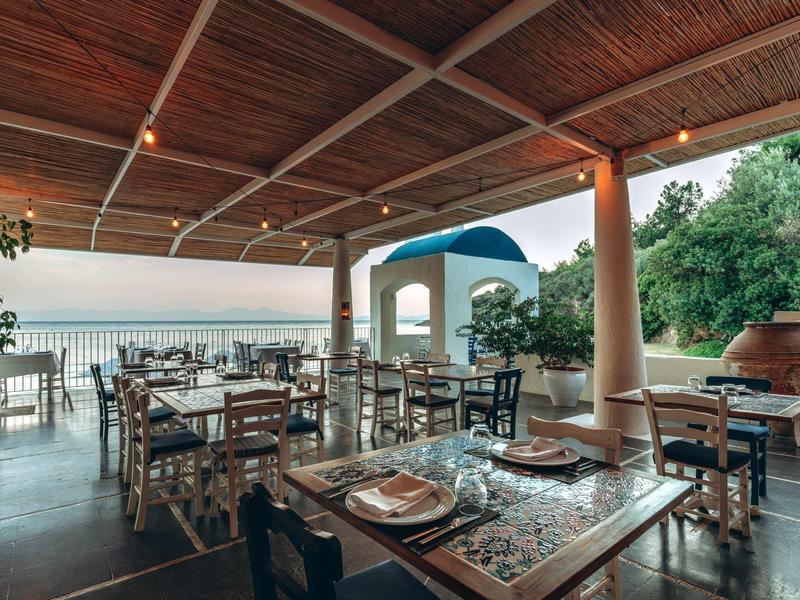 Offener Restaurantbereich mit Holzdach und rustikalen Holztischen, Blick aufs Meer bei Abendlicht.
