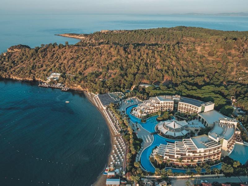 Große Hotelanlage mit Pools am bewaldeten Küstenabschnitt und Sandstrand am blauen Meer.