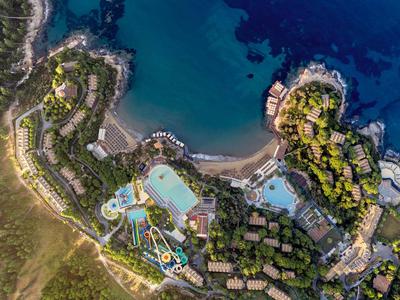 Luftaufnahme eines Hotelresorts mit Pools und Meer, umgeben von grünem Gelände.