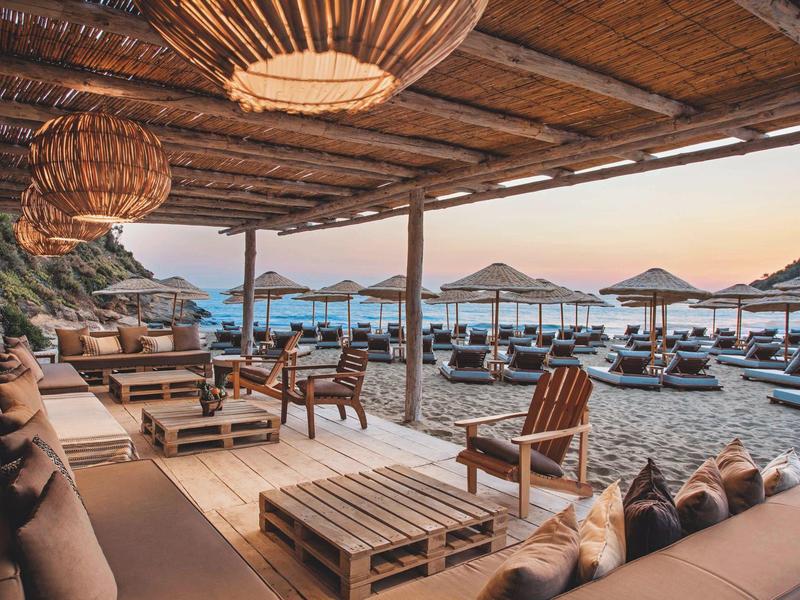 Accogliente lounge sulla spiaggia con mobili in legno e ombrelloni al tramonto.