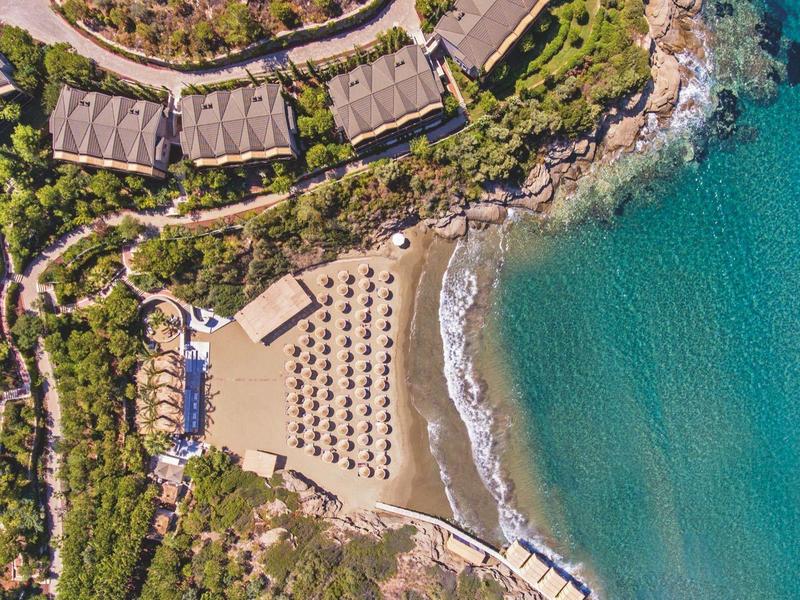Veduta aerea di un resort sulla spiaggia con lettini, ombrelloni e mare turchese.
