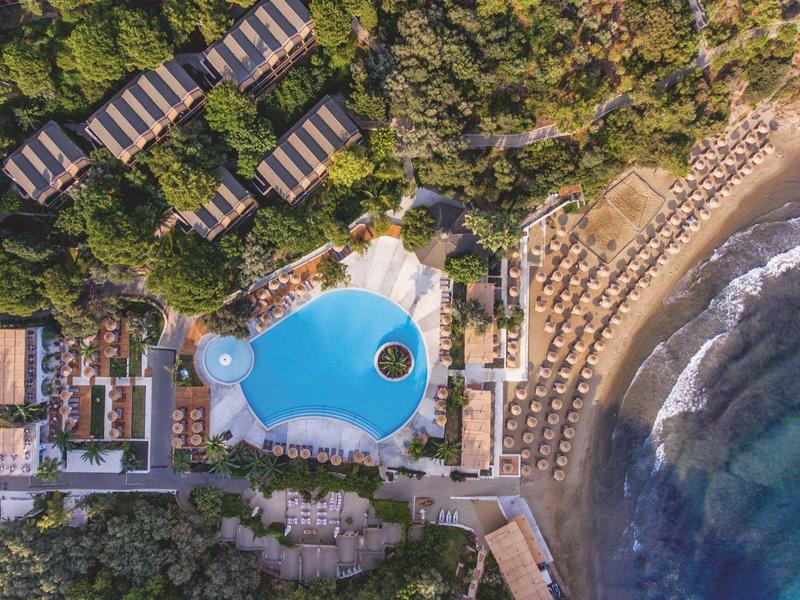 Vista aerea di un resort sulla spiaggia con piscina, lettini e ombrelloni vicino al mare.