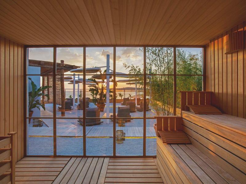 Vista al tramonto da una sauna in legno che dà su un salotto all'aperto con ombrelloni e sedie.