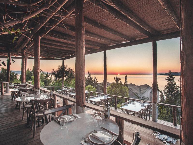 Vista al tramonto da una terrazza in legno con tavoli apparecchiati.