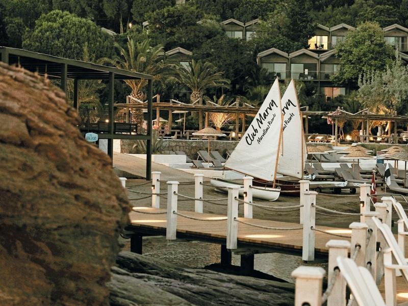 Barca a vela attraccata a un molo in una località turistica in legno verde con ombrelloni e case