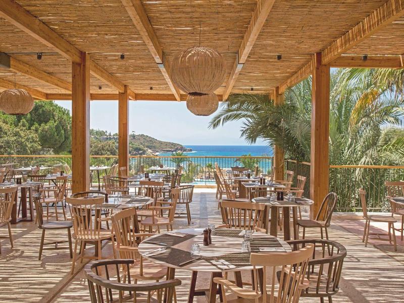 Ampio terrazzo in legno con tavoli rotondi e sedie, vista sul mare.