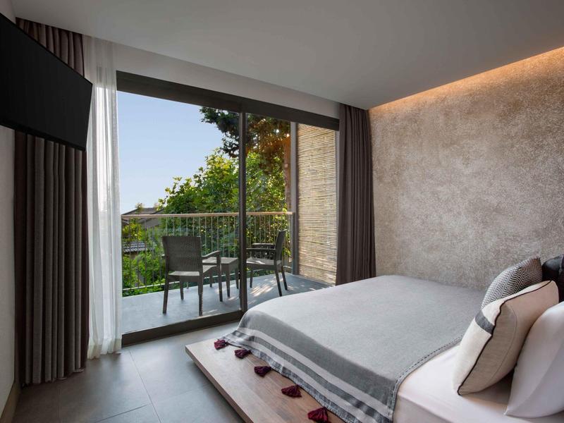 Camera d'hotel moderna con letto grande, porte scorrevoli e balcone con vista sul verde.