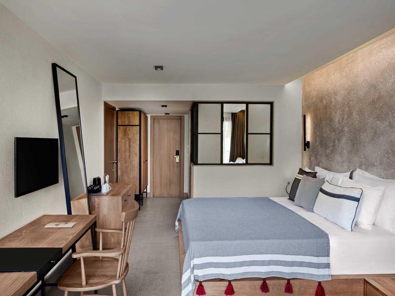 Camera d'hotel moderna con letto grande, mobili in legno e parete grigia strutturata.