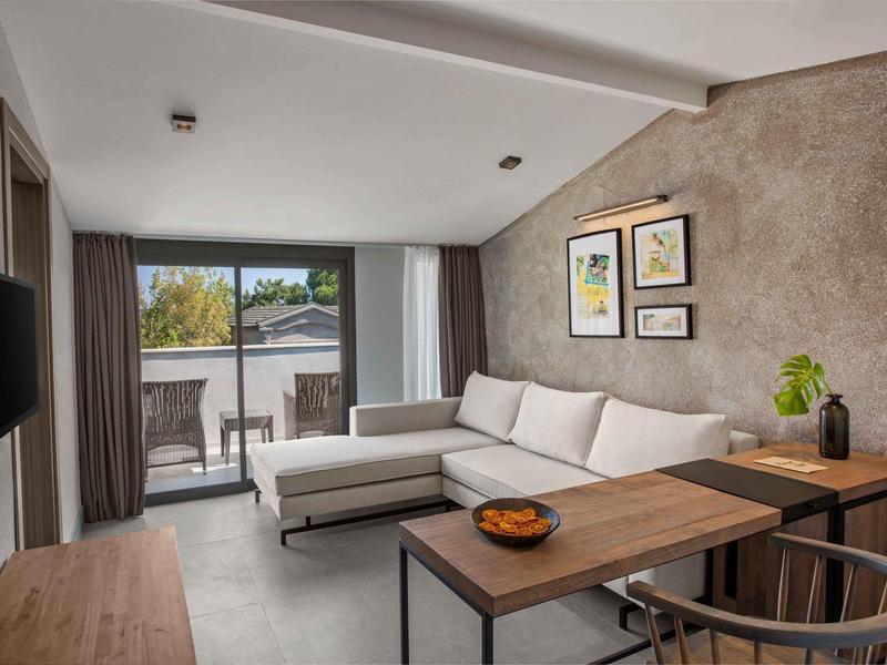 Soggiorno moderno con divano bianco, tavolo in legno e porta a vetri verso balcone.