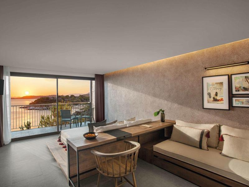 Camera d'hotel moderna con divano, scrivania e grande finestra con vista sul mare al tramonto