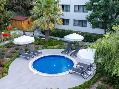 Kleiner runder Pool mit weißen Sonnenschirmen und Liegestühlen in einem grünen Hotelgarten.