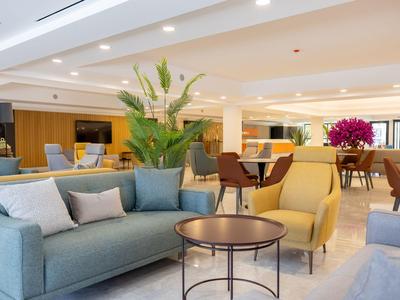 Helle Hotellounge mit modernen Sitzmöbeln, Tischen und Pflanzen als Dekoration.