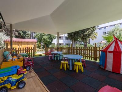 Kinderspielbereich mit bunten Tischen, Stühlen, Spielzeugfahrzeugen und einem kleinen Zirkuszelt.