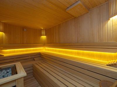 Helle, moderne Sauna mit Holzverkleidung, Eckbänken und warmem LED-Licht.